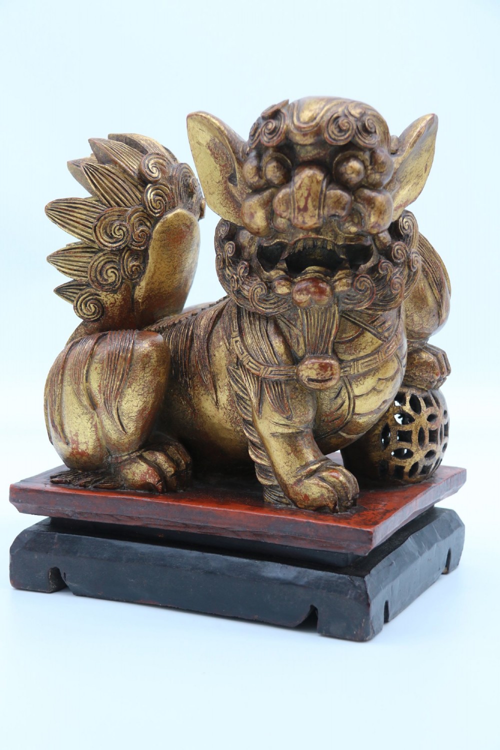 A pair of hand-carved Chinese wooden guardian lions finished in gold gilding and red lacquer, seated on dark rectangular bases. View VI