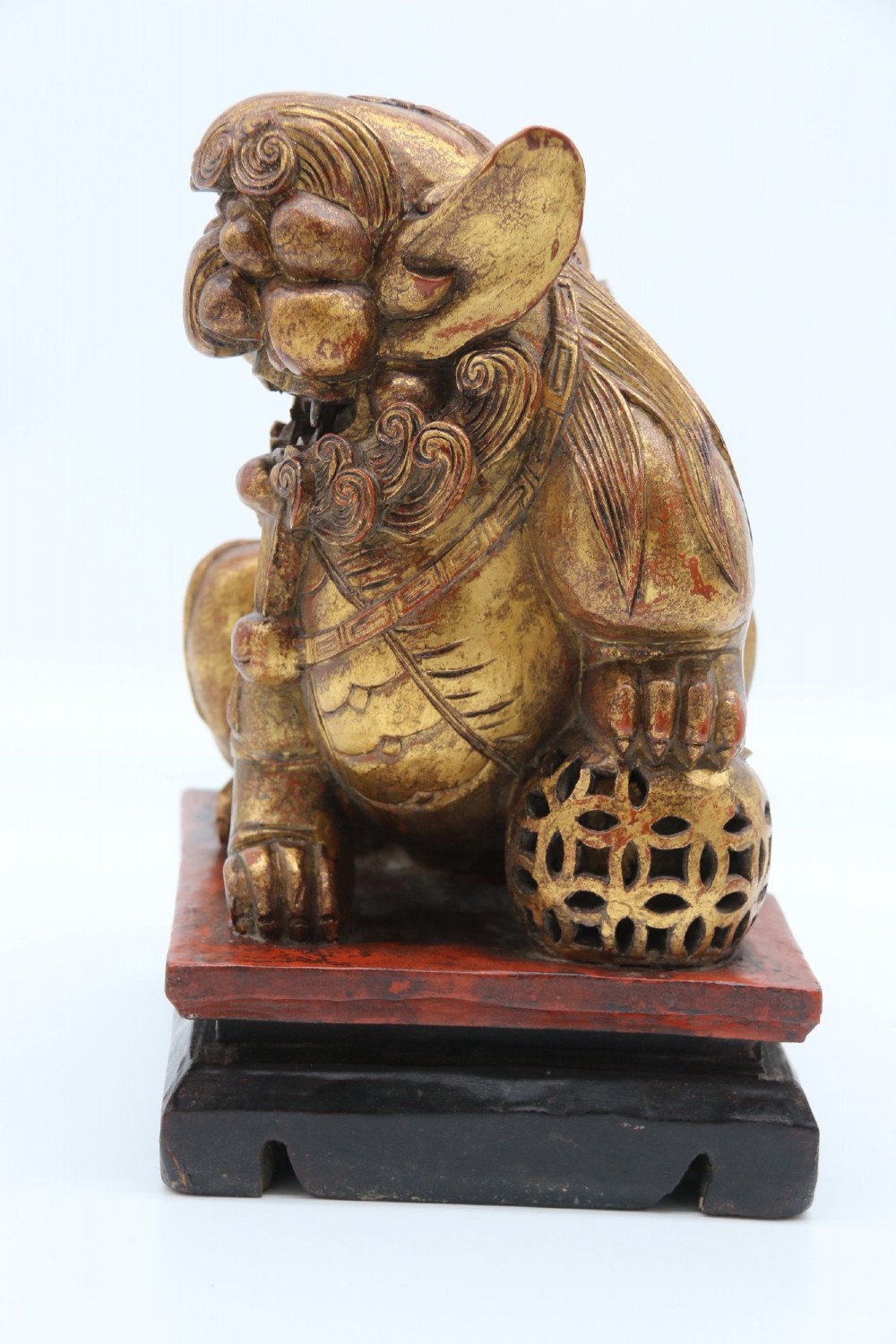 A pair of hand-carved Chinese wooden guardian lions finished in gold gilding and red lacquer, seated on dark rectangular bases. View VII