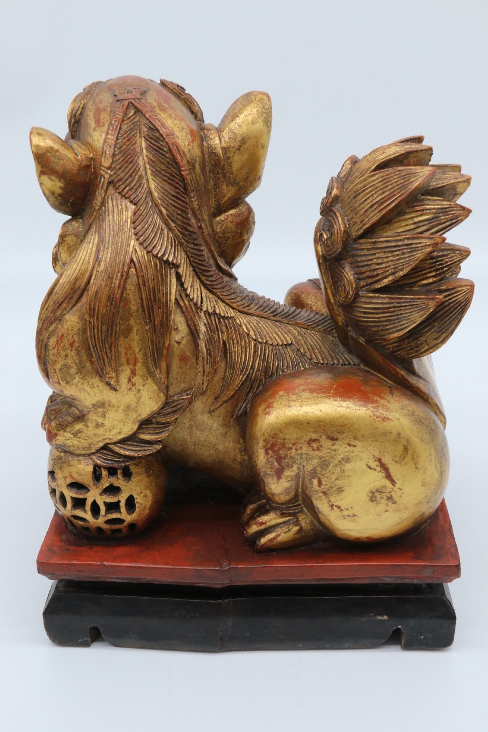 A pair of hand-carved Chinese wooden guardian lions finished in gold gilding and red lacquer, seated on dark rectangular bases. View XII