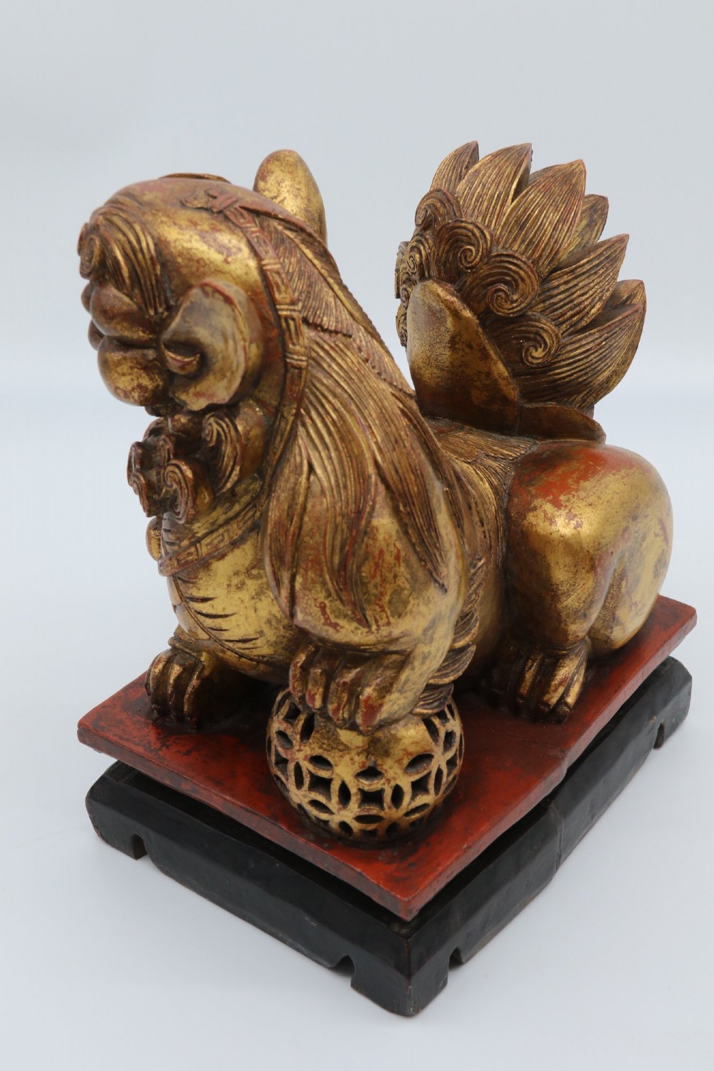 A pair of hand-carved Chinese wooden guardian lions finished in gold gilding and red lacquer, seated on dark rectangular bases. View XIII