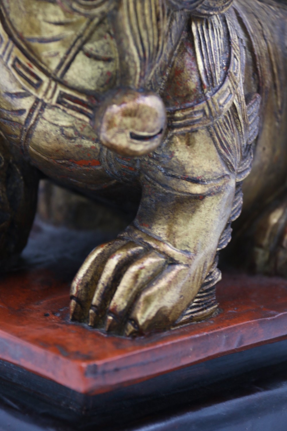 A pair of hand-carved Chinese wooden guardian lions finished in gold gilding and red lacquer, seated on dark rectangular bases. View XIV