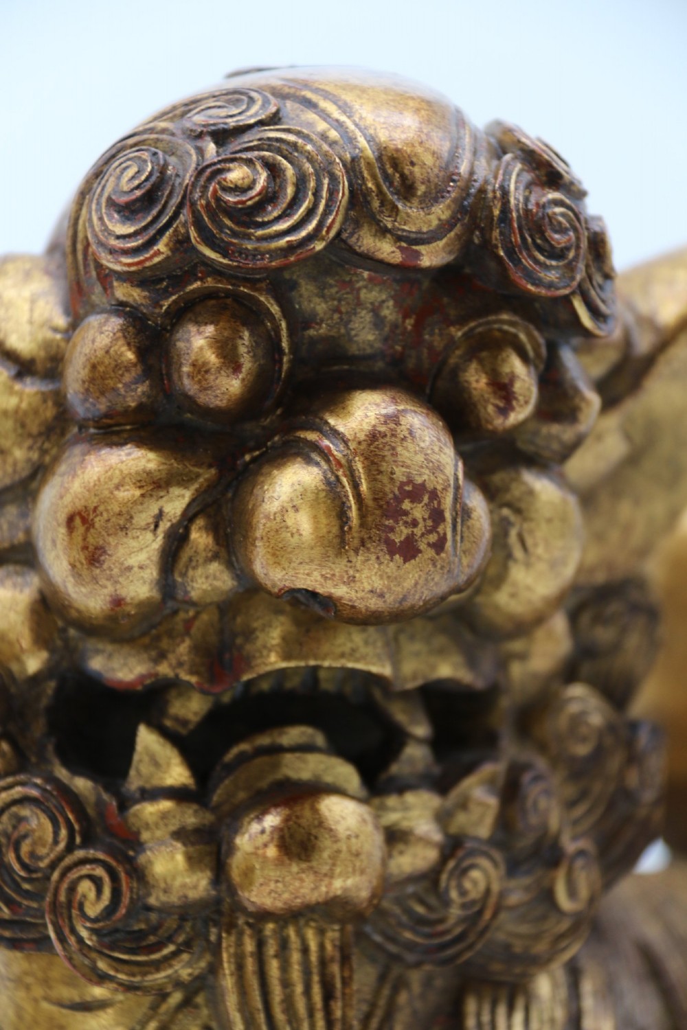 A pair of hand-carved Chinese wooden guardian lions finished in gold gilding and red lacquer, seated on dark rectangular bases. View XV