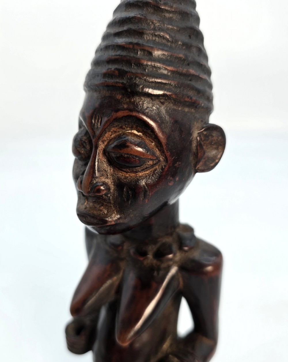 A dark brown hand-carved wooden figure depicting a kneeling female with a tall ridged headpiece and carved facial markings. View IX