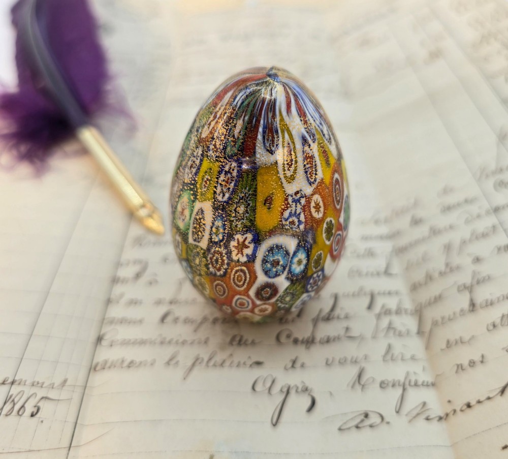An egg-shaped Murano glass paperweight featuring colourful millefiori cane patterns and gold aventurine inclusions throughout.