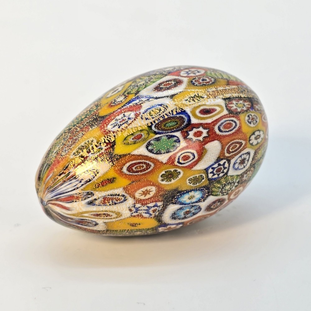 An egg-shaped Murano glass paperweight featuring colourful millefiori cane patterns and gold aventurine inclusions throughout. View VI