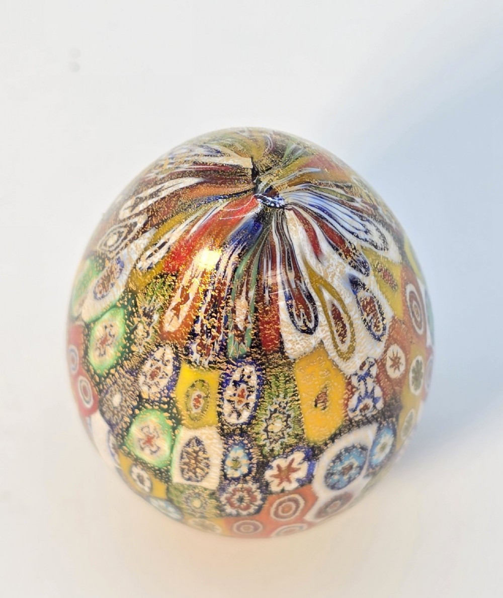 An egg-shaped Murano glass paperweight featuring colourful millefiori cane patterns and gold aventurine inclusions throughout. View VII