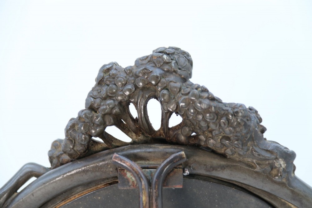 An Art Nouveau pewter table mirror featuring an asymmetrical botanical frame with organic crests and an easel back support. View X