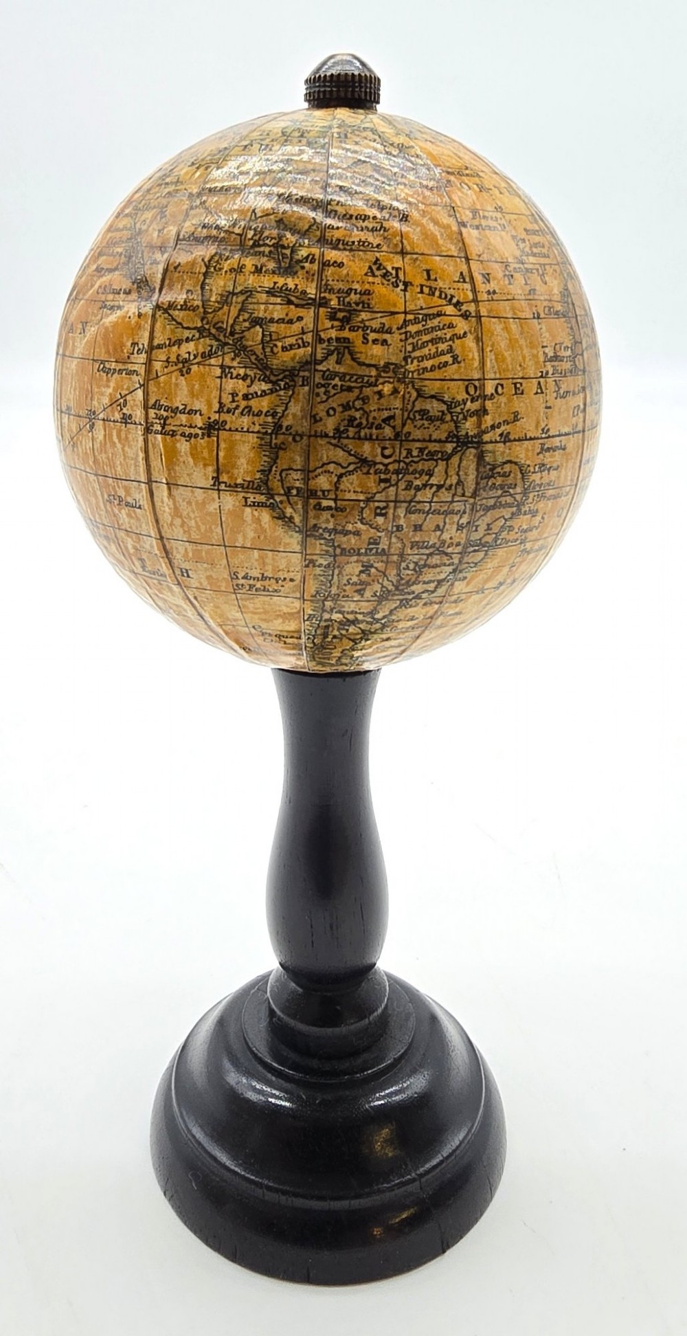 A miniature terrestrial globe with printed sepia paper gores resting on a turned black ebonised wooden pedestal stand with a metal top finial.