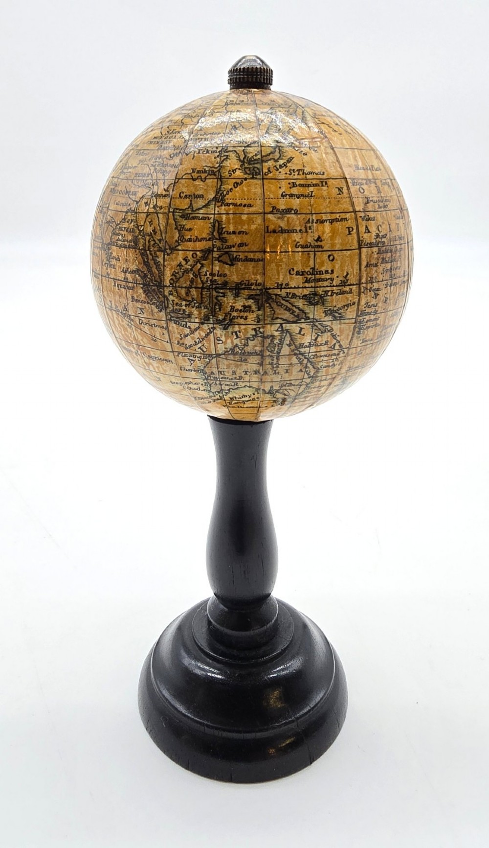 A miniature terrestrial globe with printed sepia paper gores resting on a turned black ebonised wooden pedestal stand with a metal top finial. View IV