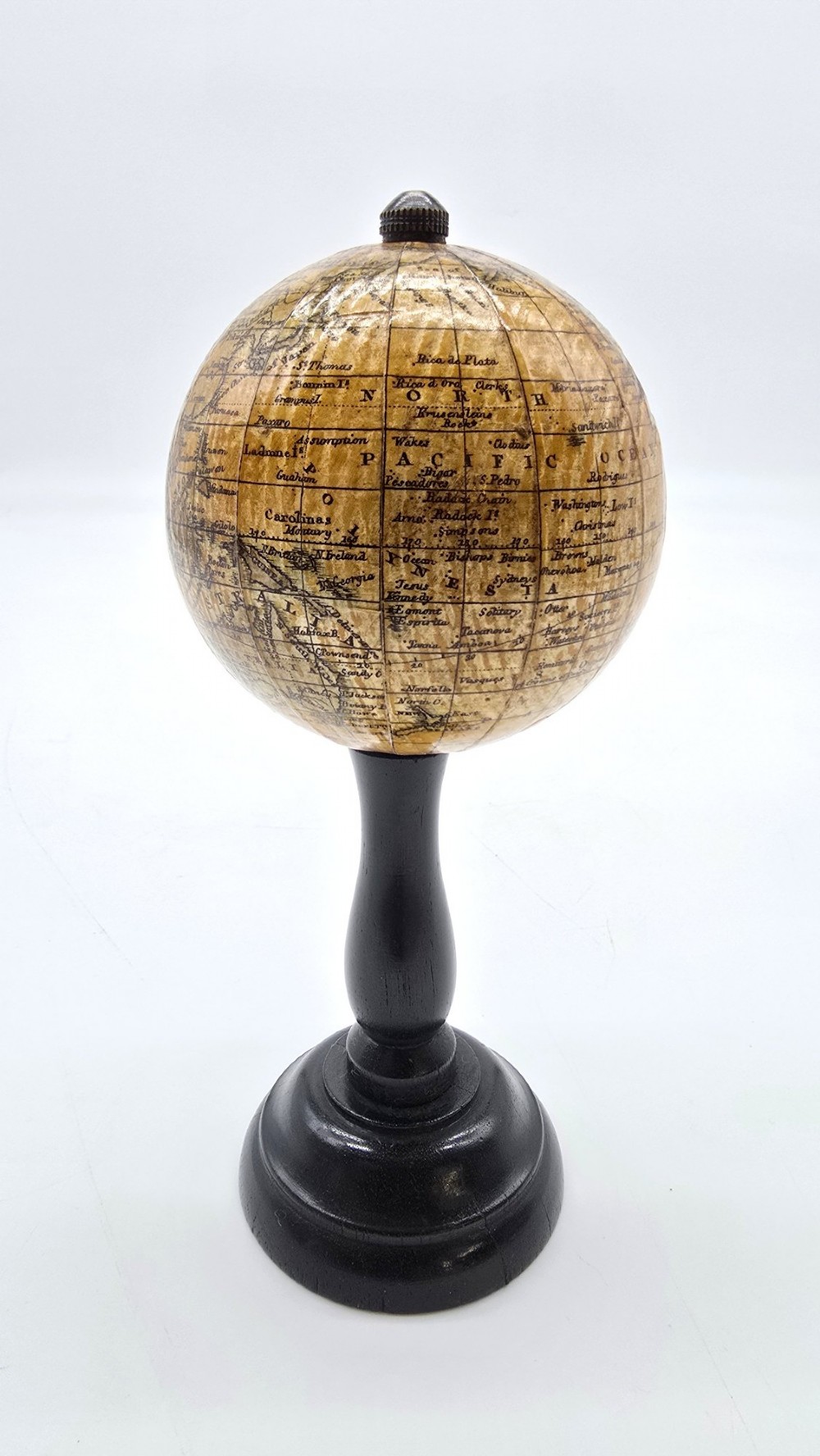 A miniature terrestrial globe with printed sepia paper gores resting on a turned black ebonised wooden pedestal stand with a metal top finial. View V