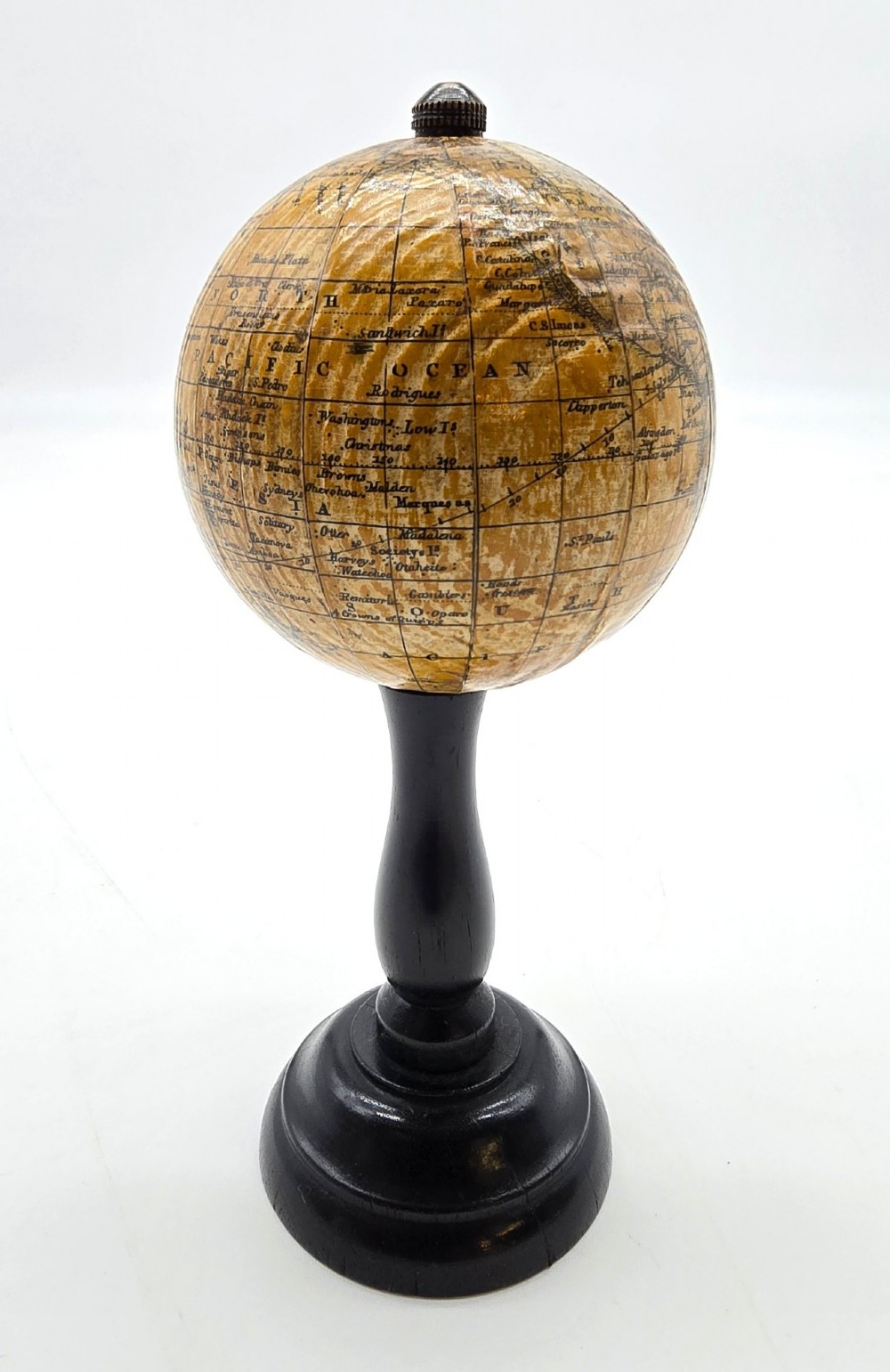 A miniature terrestrial globe with printed sepia paper gores resting on a turned black ebonised wooden pedestal stand with a metal top finial. View VI
