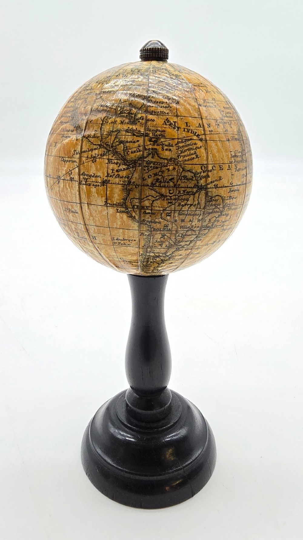 A miniature terrestrial globe with printed sepia paper gores resting on a turned black ebonised wooden pedestal stand with a metal top finial. View VII