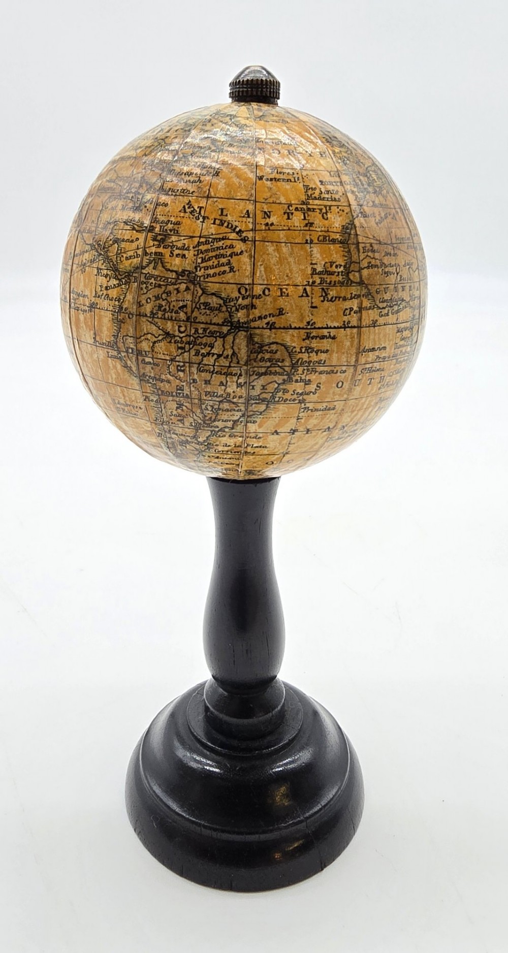 A miniature terrestrial globe with printed sepia paper gores resting on a turned black ebonised wooden pedestal stand with a metal top finial. View VIII