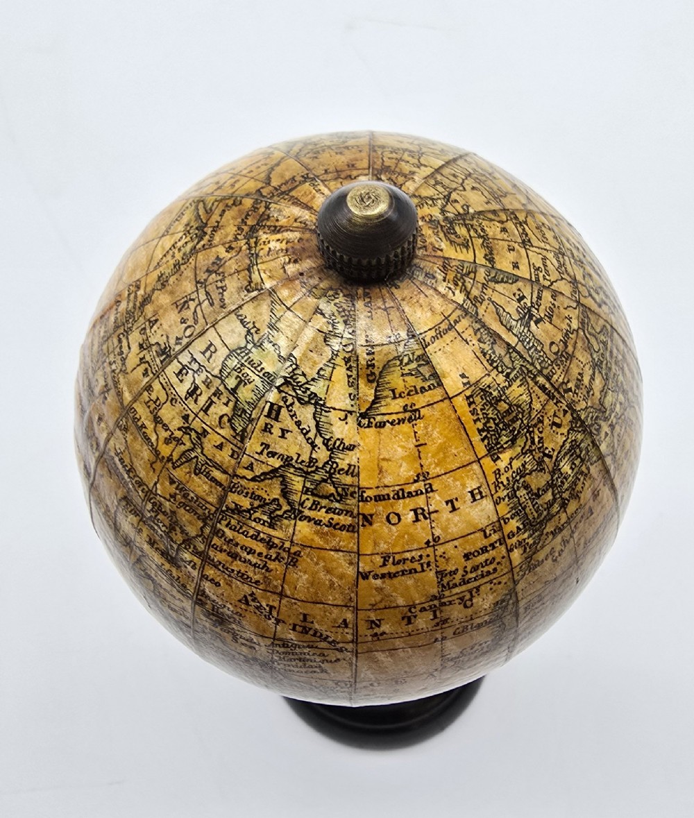 A miniature terrestrial globe with printed sepia paper gores resting on a turned black ebonised wooden pedestal stand with a metal top finial. View IX
