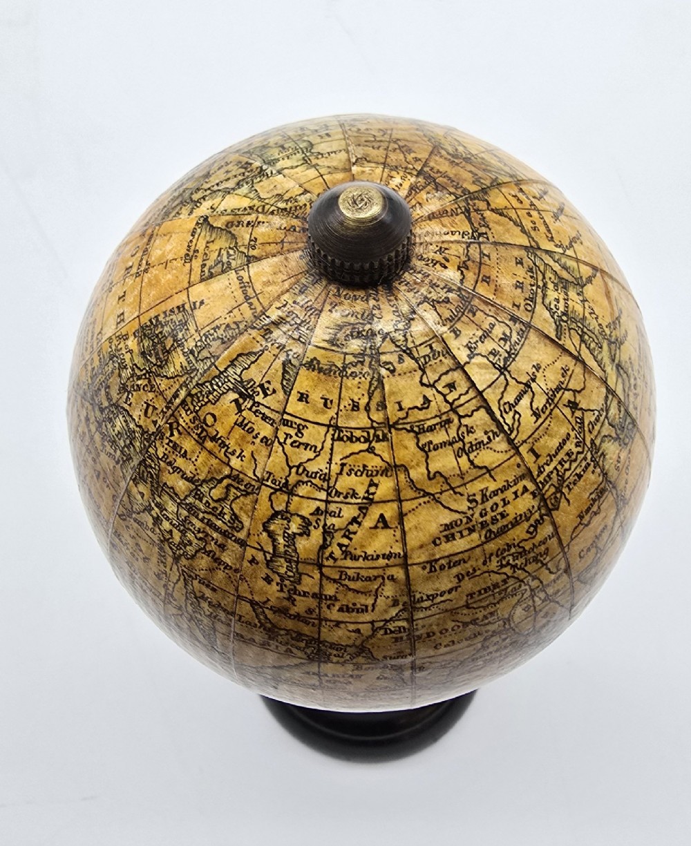 A miniature terrestrial globe with printed sepia paper gores resting on a turned black ebonised wooden pedestal stand with a metal top finial. View X