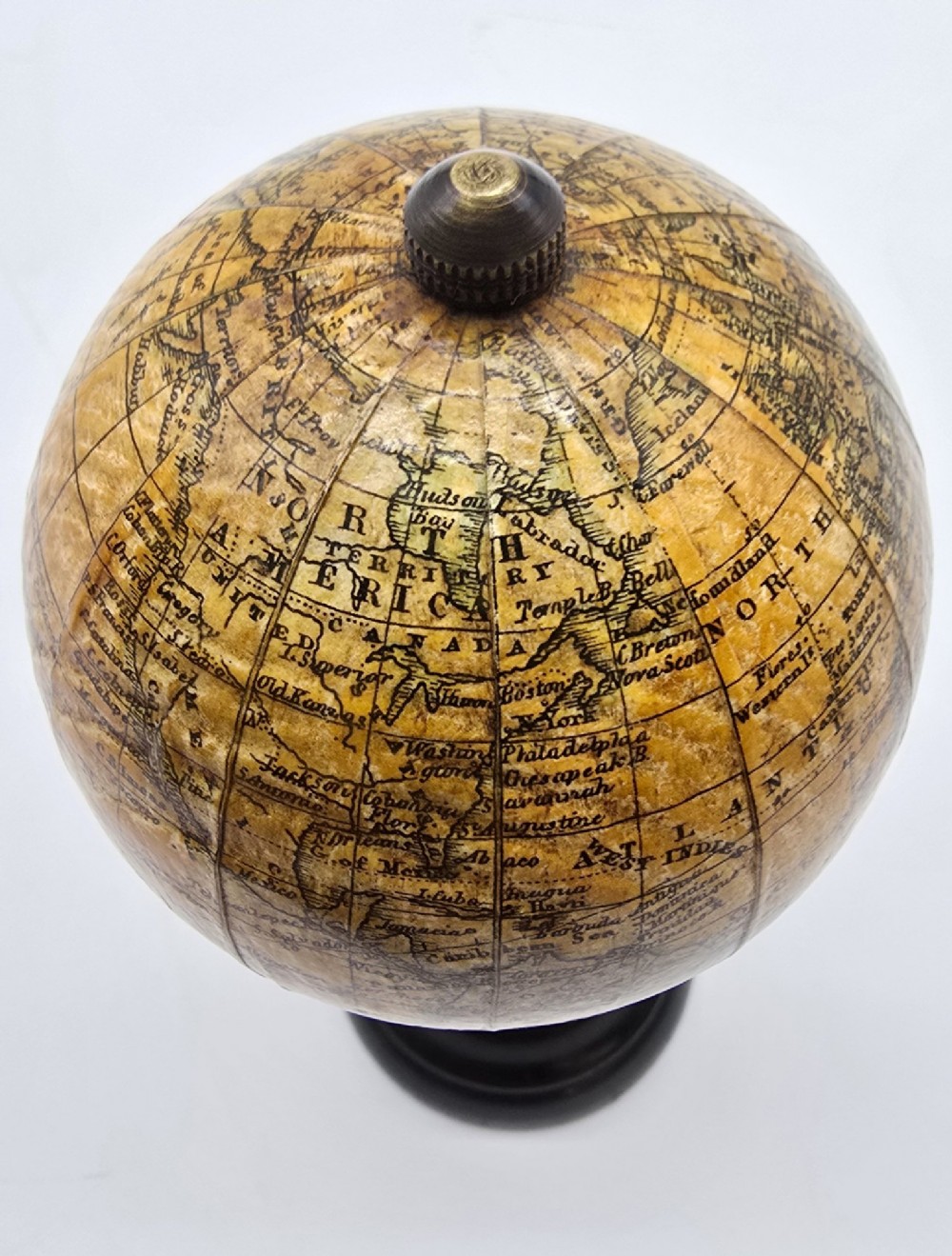 A miniature terrestrial globe with printed sepia paper gores resting on a turned black ebonised wooden pedestal stand with a metal top finial. View XI
