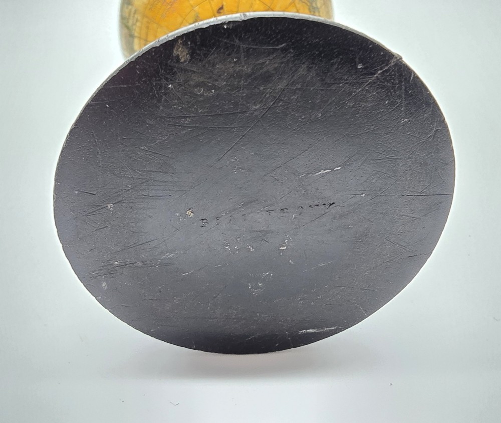 A miniature terrestrial globe with printed sepia paper gores resting on a turned black ebonised wooden pedestal stand with a metal top finial. View XII