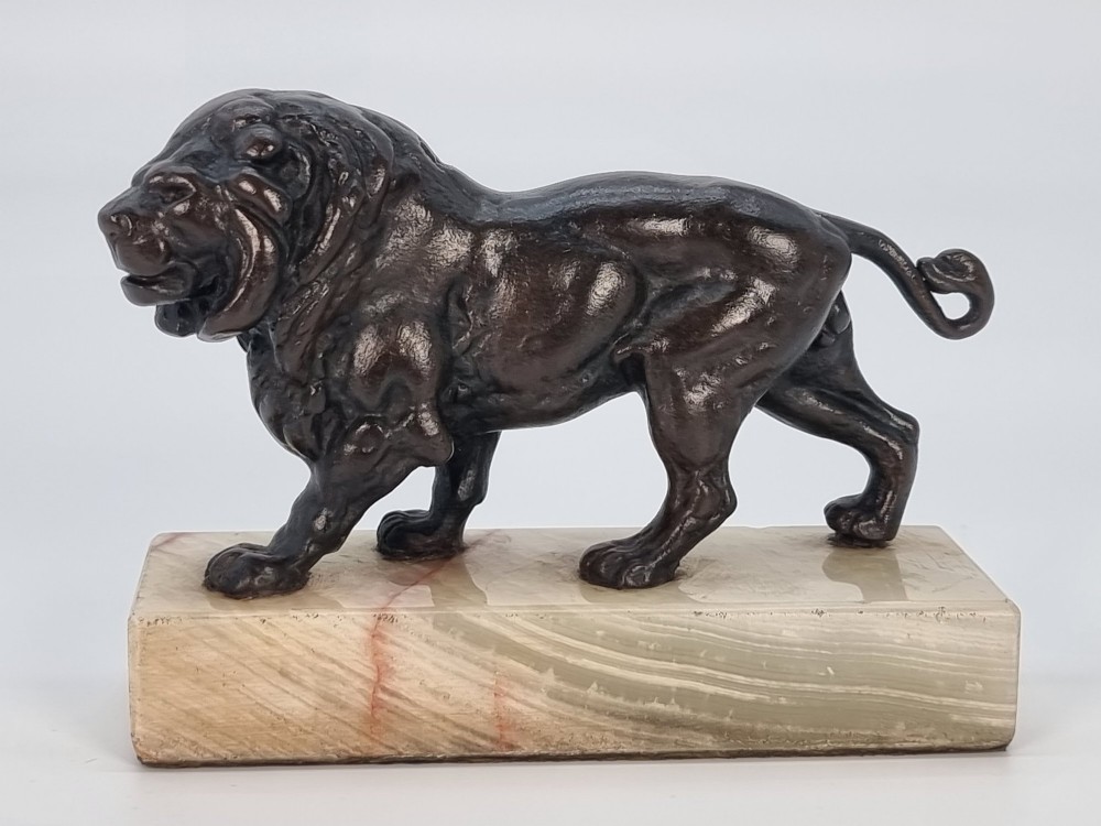 A dark patinated bronze sculpture of a prowling lion mounted on a rectangular cream veined onyx base.