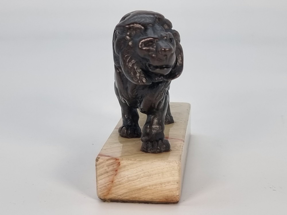 A dark patinated bronze sculpture of a prowling lion mounted on a rectangular cream veined onyx base. View III