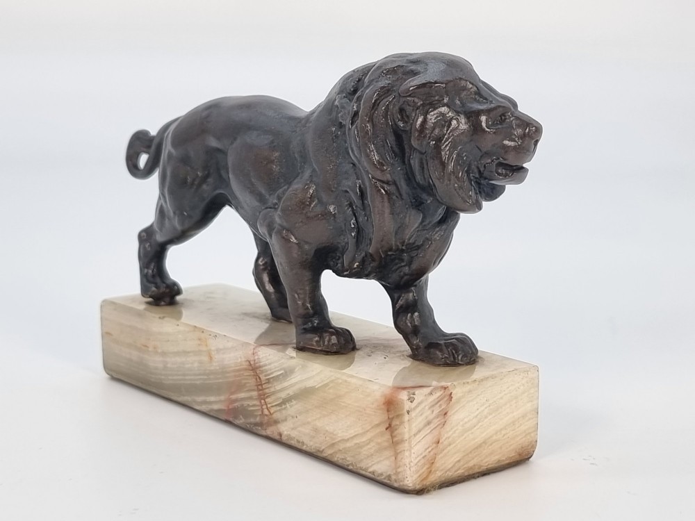 A dark patinated bronze sculpture of a prowling lion mounted on a rectangular cream veined onyx base. View IV