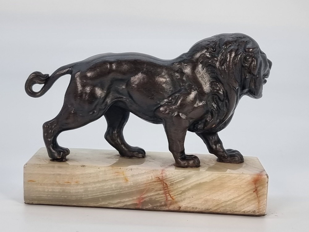 A dark patinated bronze sculpture of a prowling lion mounted on a rectangular cream veined onyx base. View V