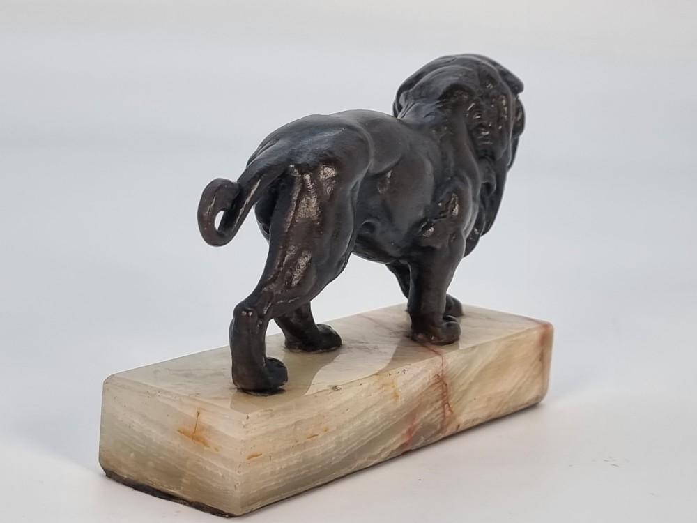 A dark patinated bronze sculpture of a prowling lion mounted on a rectangular cream veined onyx base. View VI