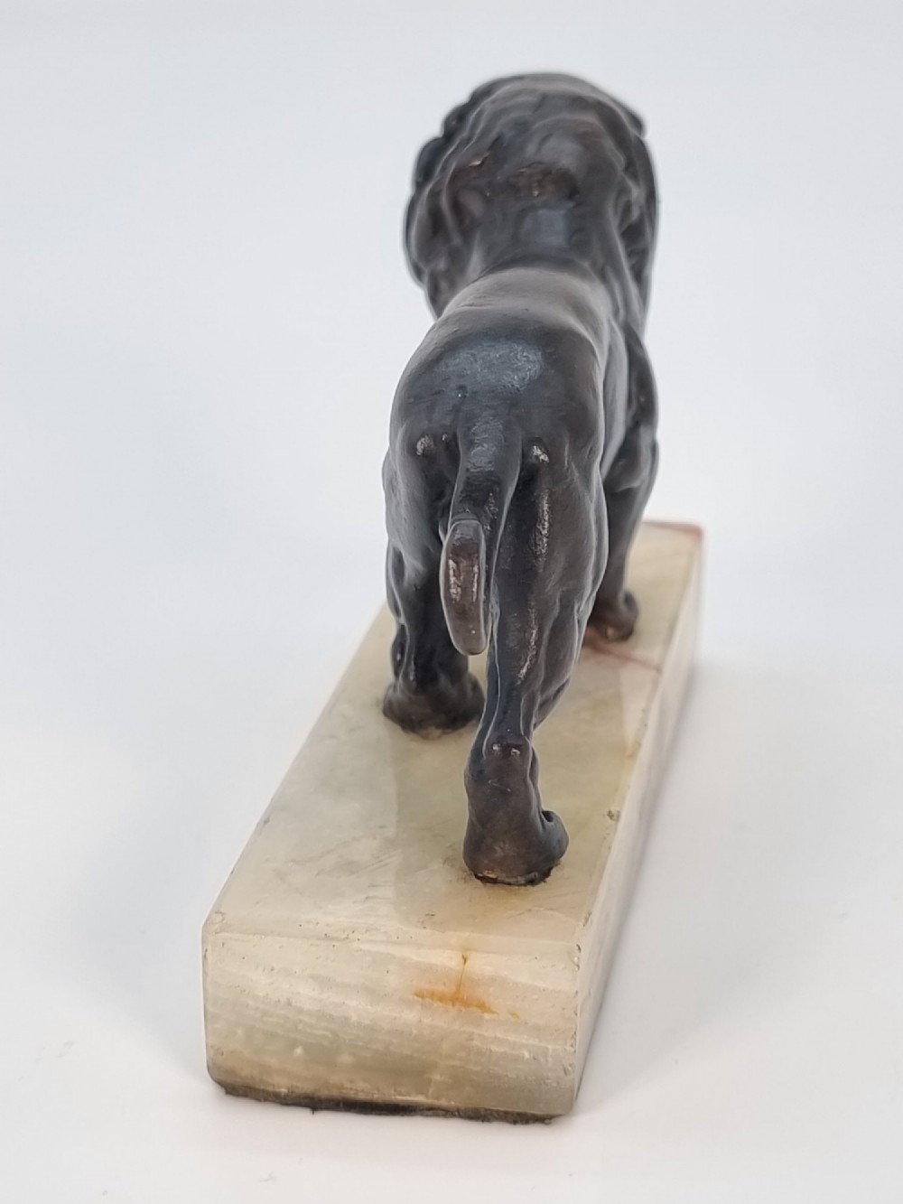 A dark patinated bronze sculpture of a prowling lion mounted on a rectangular cream veined onyx base. View VII