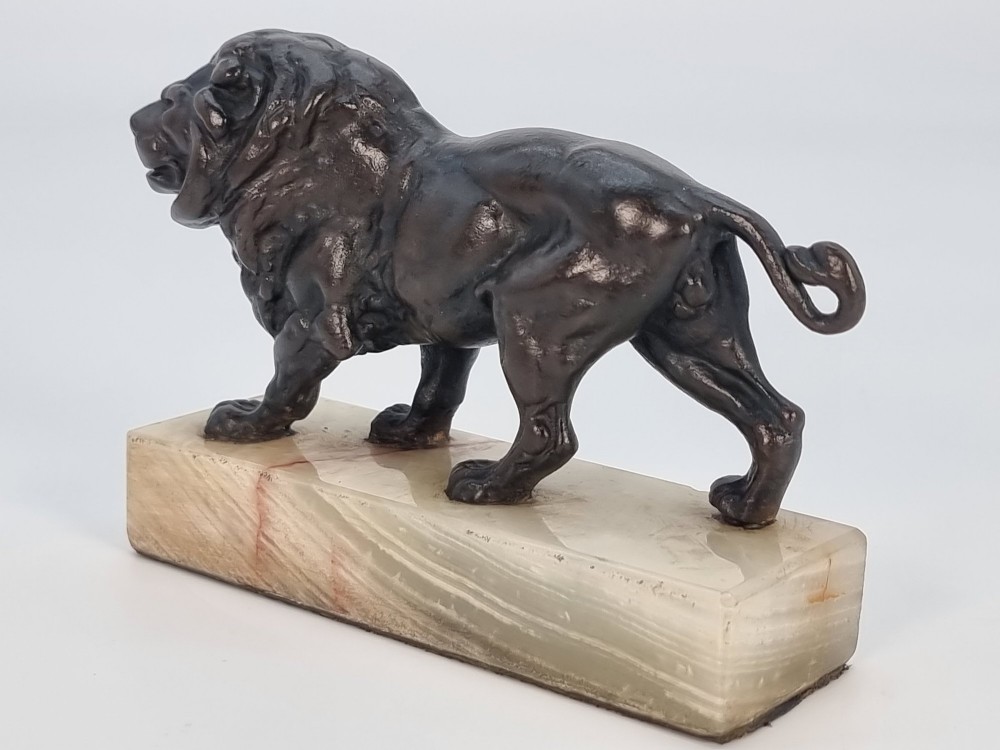A dark patinated bronze sculpture of a prowling lion mounted on a rectangular cream veined onyx base. View VIII
