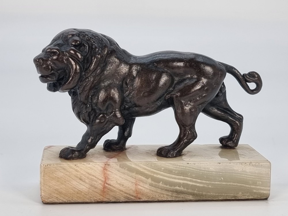 A dark patinated bronze sculpture of a prowling lion mounted on a rectangular cream veined onyx base. View IX