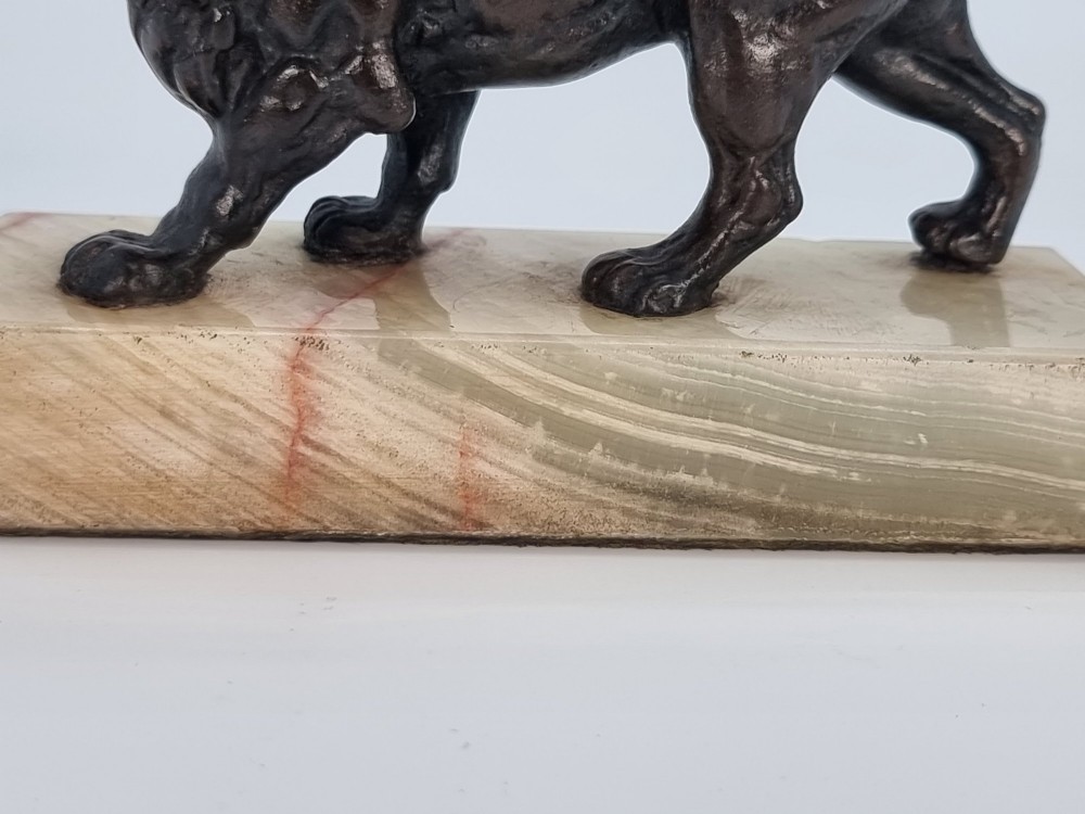 A dark patinated bronze sculpture of a prowling lion mounted on a rectangular cream veined onyx base. View XII