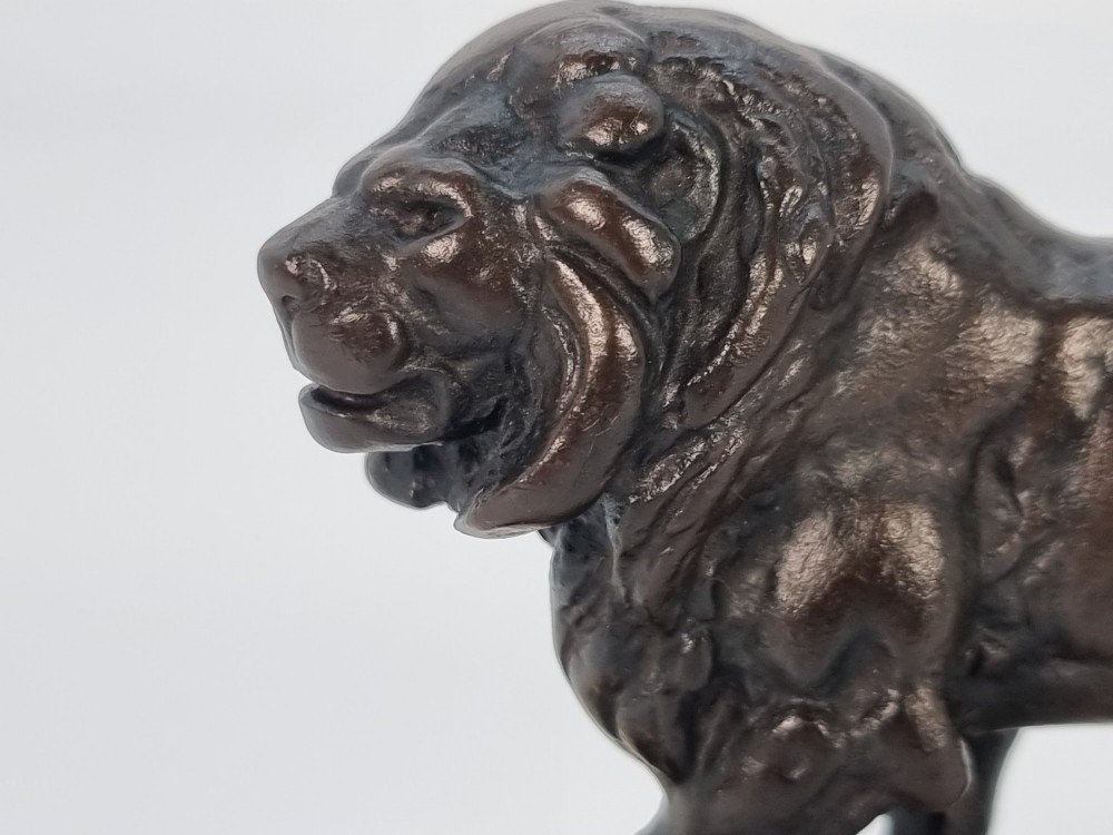 A dark patinated bronze sculpture of a prowling lion mounted on a rectangular cream veined onyx base. View XIII