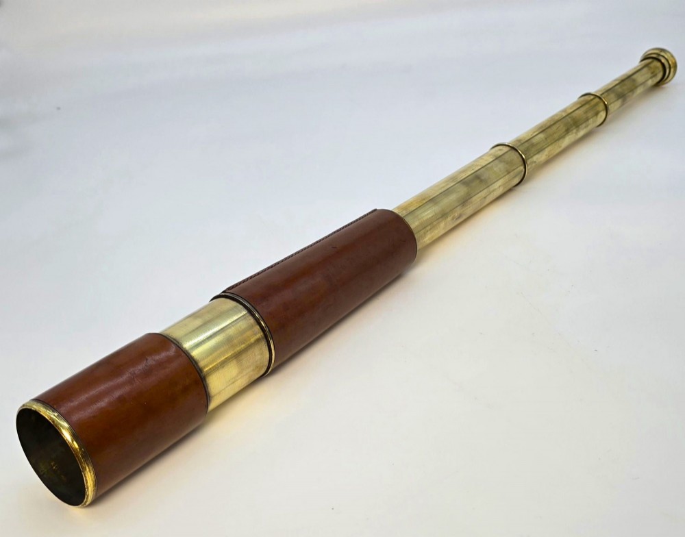 A brass multi-draw military telescope featuring stitched brown leather protective sleeves along the barrel.