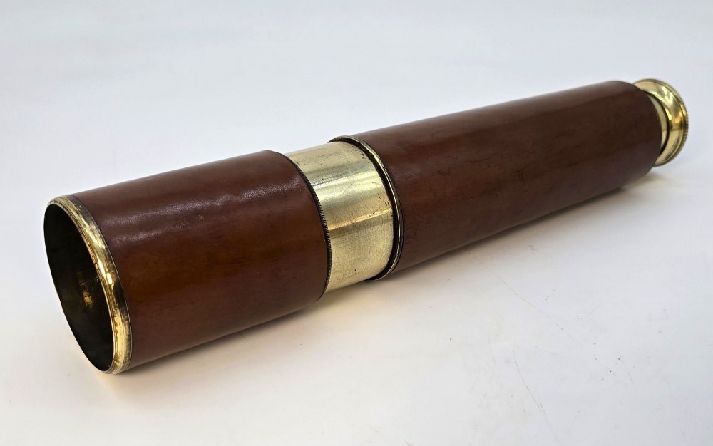 A brass multi-draw military telescope featuring stitched brown leather protective sleeves along the barrel. View X