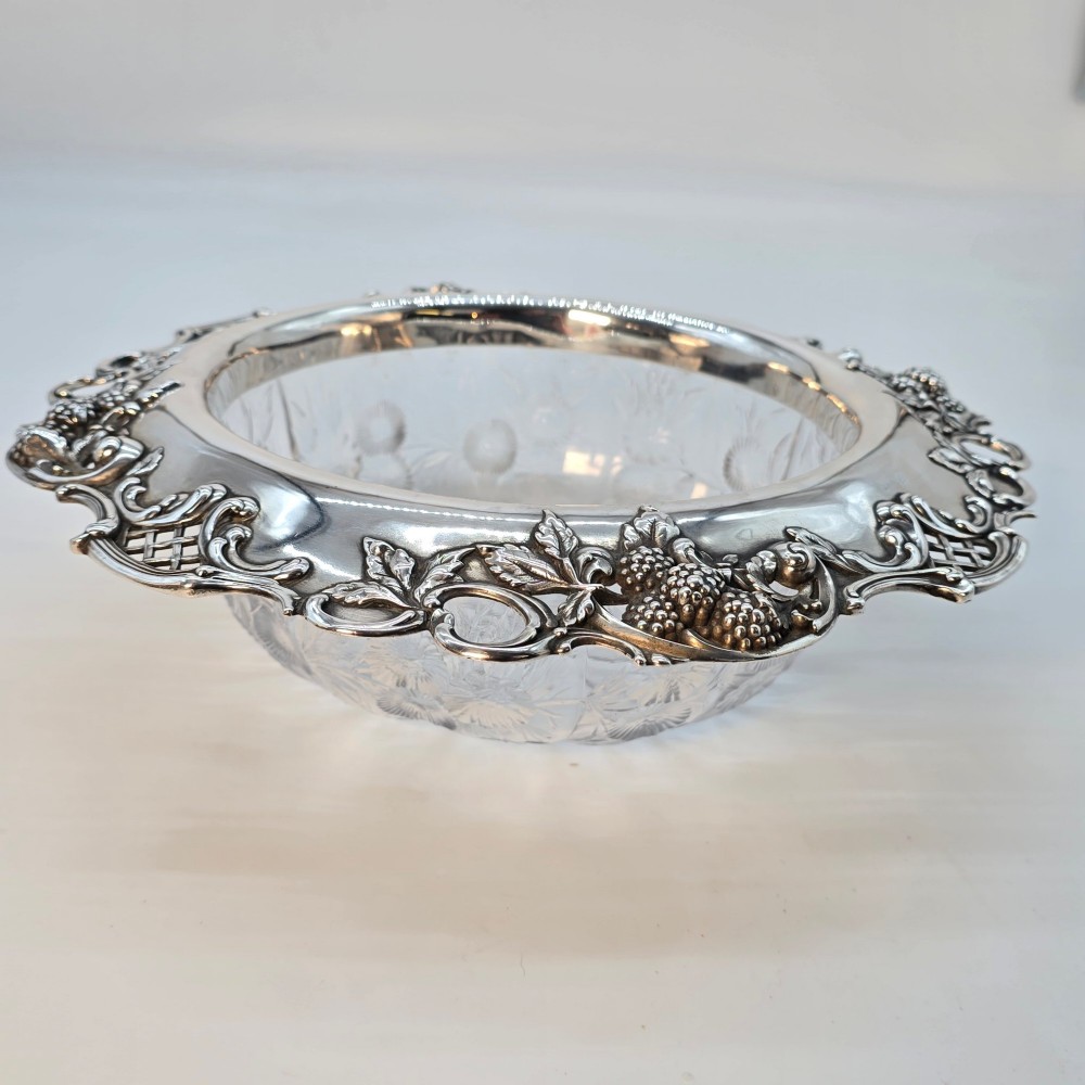 A clear crystal bowl featuring an intricately chased sterling silver rim decorated with floral motifs, scrolls, and lattice patterns.