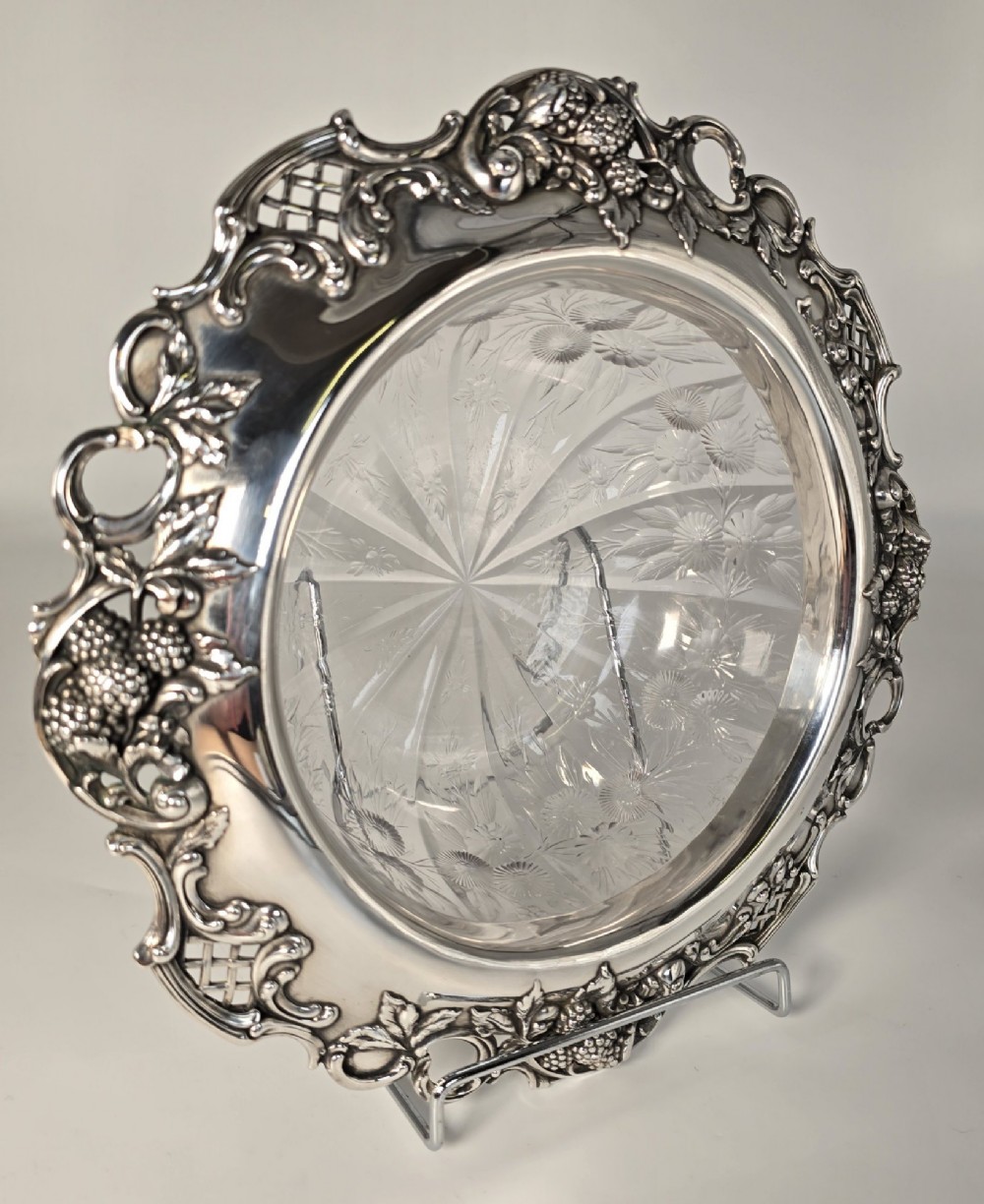 A clear crystal bowl featuring an intricately chased sterling silver rim decorated with floral motifs, scrolls, and lattice patterns. View II