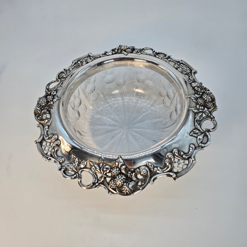 A clear crystal bowl featuring an intricately chased sterling silver rim decorated with floral motifs, scrolls, and lattice patterns. View IV
