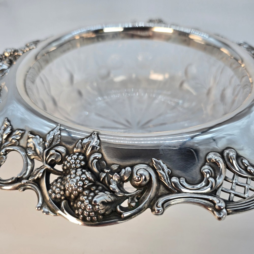 A clear crystal bowl featuring an intricately chased sterling silver rim decorated with floral motifs, scrolls, and lattice patterns. View IX