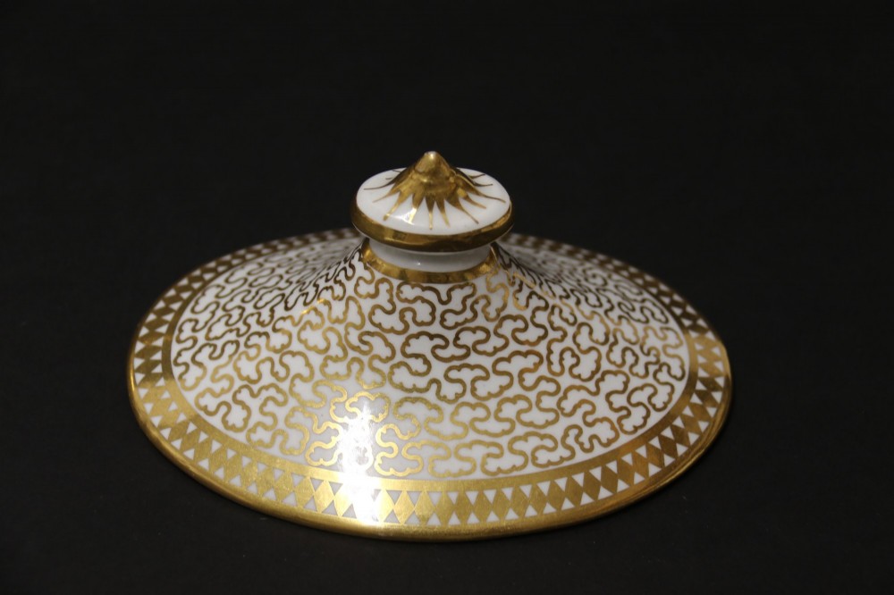 An antique white porcelain covered sucrier decorated with intricate gold scroll patterning, geometric trim, twin loop handles, and a pointed finial lid. View IX