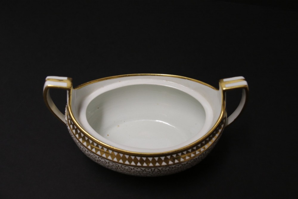 An antique white porcelain covered sucrier decorated with intricate gold scroll patterning, geometric trim, twin loop handles, and a pointed finial lid. View X