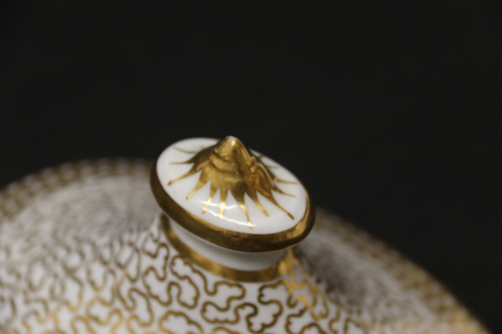 An antique white porcelain covered sucrier decorated with intricate gold scroll patterning, geometric trim, twin loop handles, and a pointed finial lid. View XI