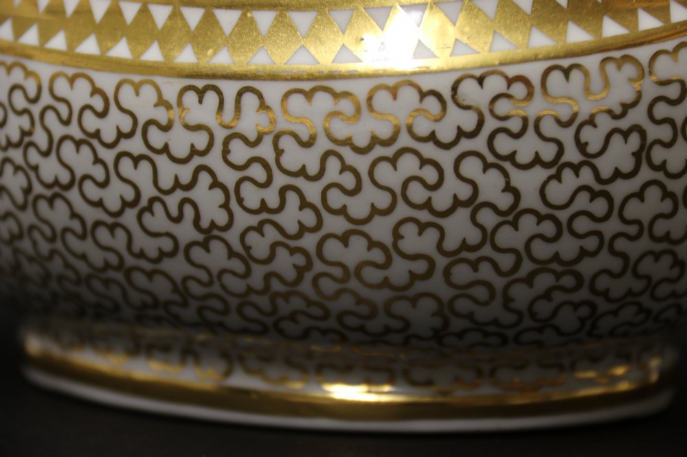 An antique white porcelain covered sucrier decorated with intricate gold scroll patterning, geometric trim, twin loop handles, and a pointed finial lid. View XII