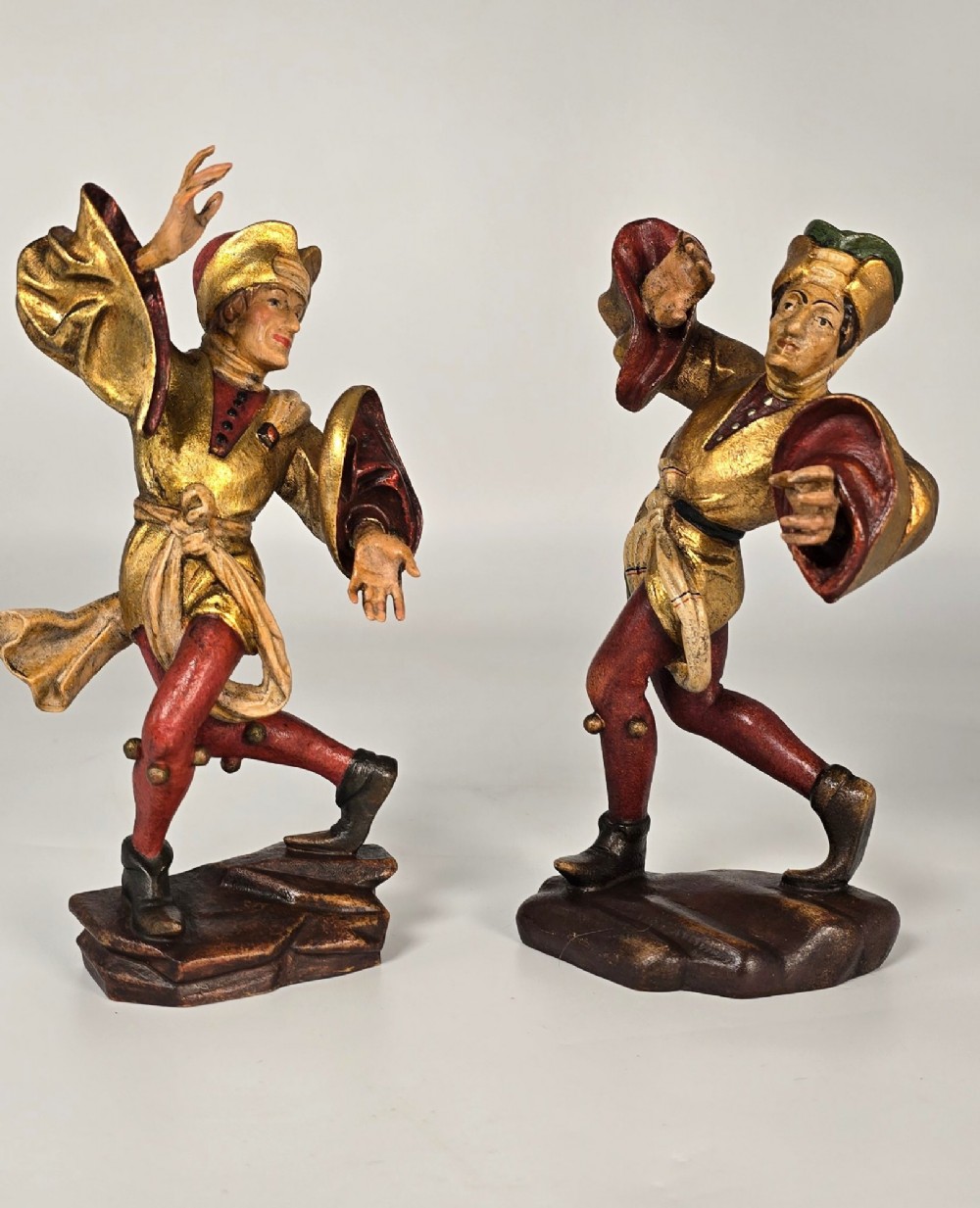 A pair of hand-carved and painted limewood figures depicting medieval dancers in gilded tunics and red hosen on carved wooden bases.