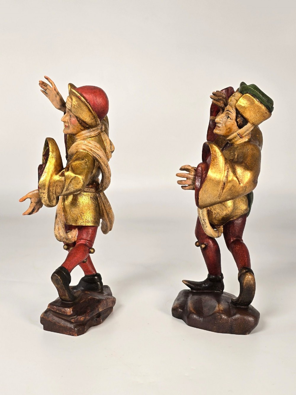 A pair of hand-carved and painted limewood figures depicting medieval dancers in gilded tunics and red hosen on carved wooden bases. View IV
