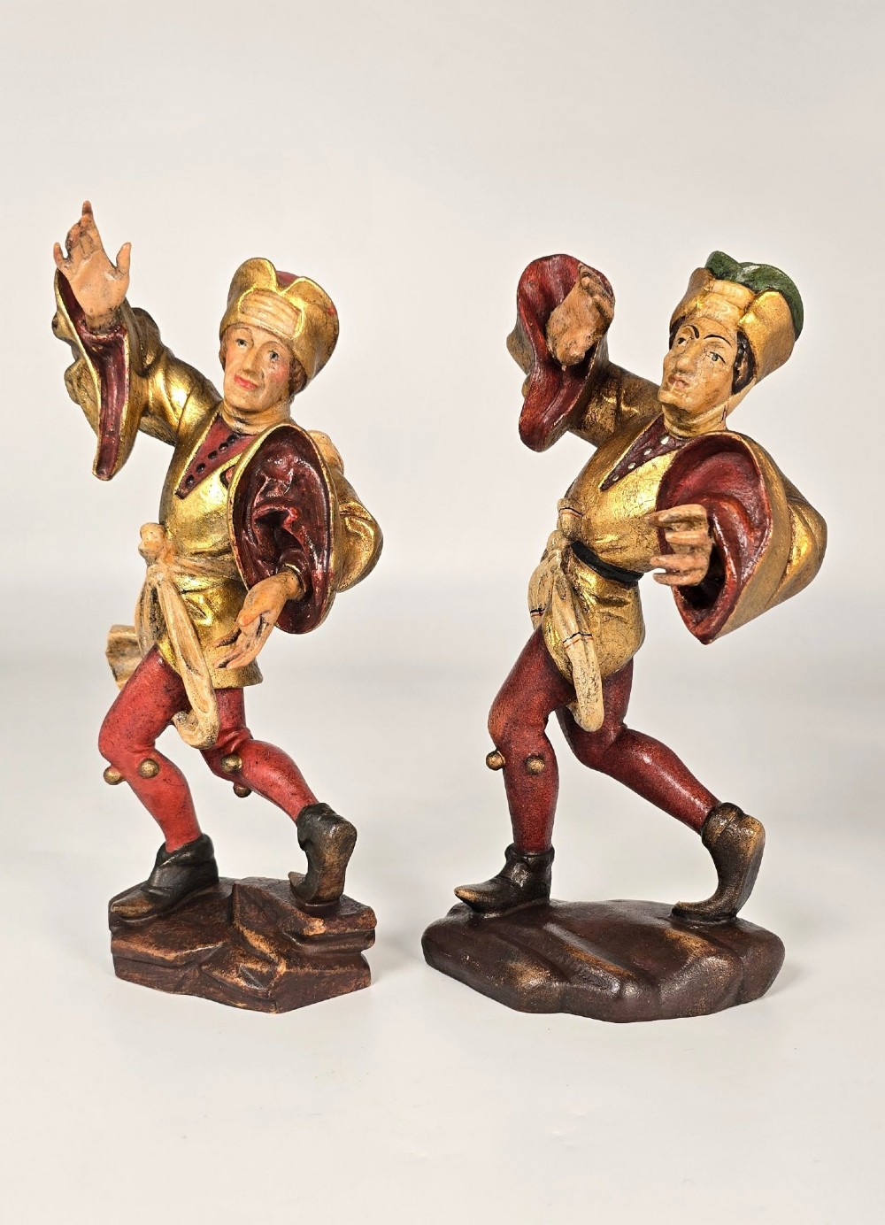 A pair of hand-carved and painted limewood figures depicting medieval dancers in gilded tunics and red hosen on carved wooden bases. View V