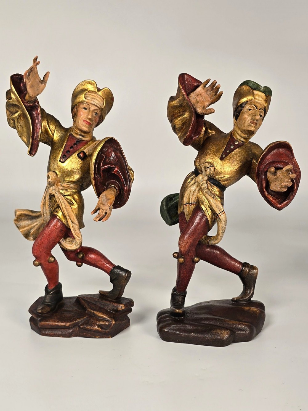 A pair of hand-carved and painted limewood figures depicting medieval dancers in gilded tunics and red hosen on carved wooden bases. View VI