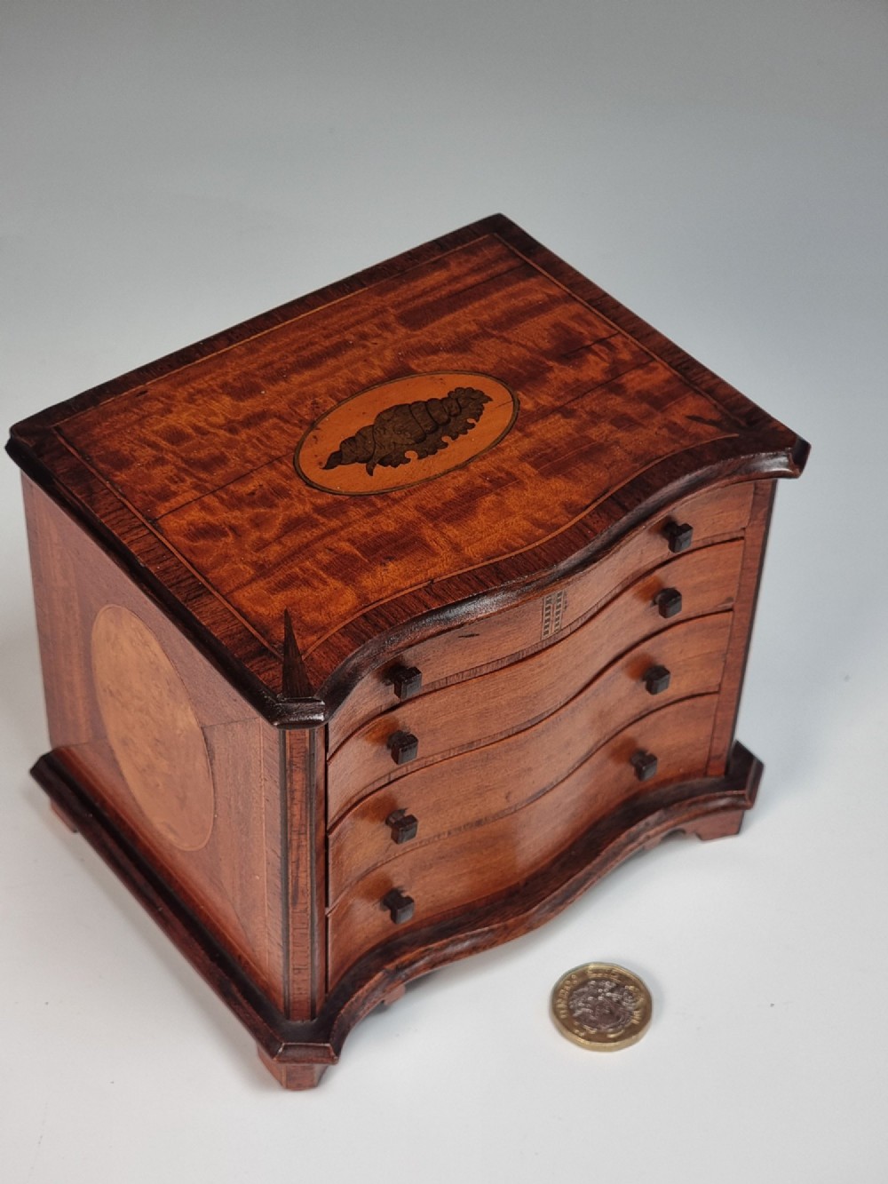 An Edwardian miniature satinwood chest of drawers featuring a serpentine front, inlaid shell medallion on the top, and four small drawers with wooden knobs. View II