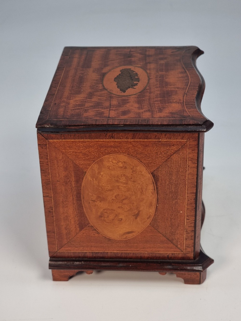 An Edwardian miniature satinwood chest of drawers featuring a serpentine front, inlaid shell medallion on the top, and four small drawers with wooden knobs. View III