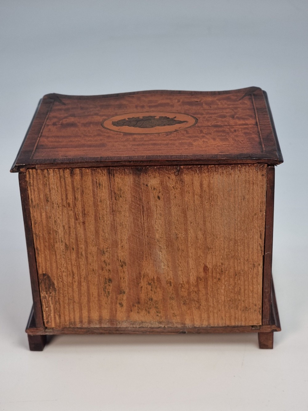 An Edwardian miniature satinwood chest of drawers featuring a serpentine front, inlaid shell medallion on the top, and four small drawers with wooden knobs. View IV