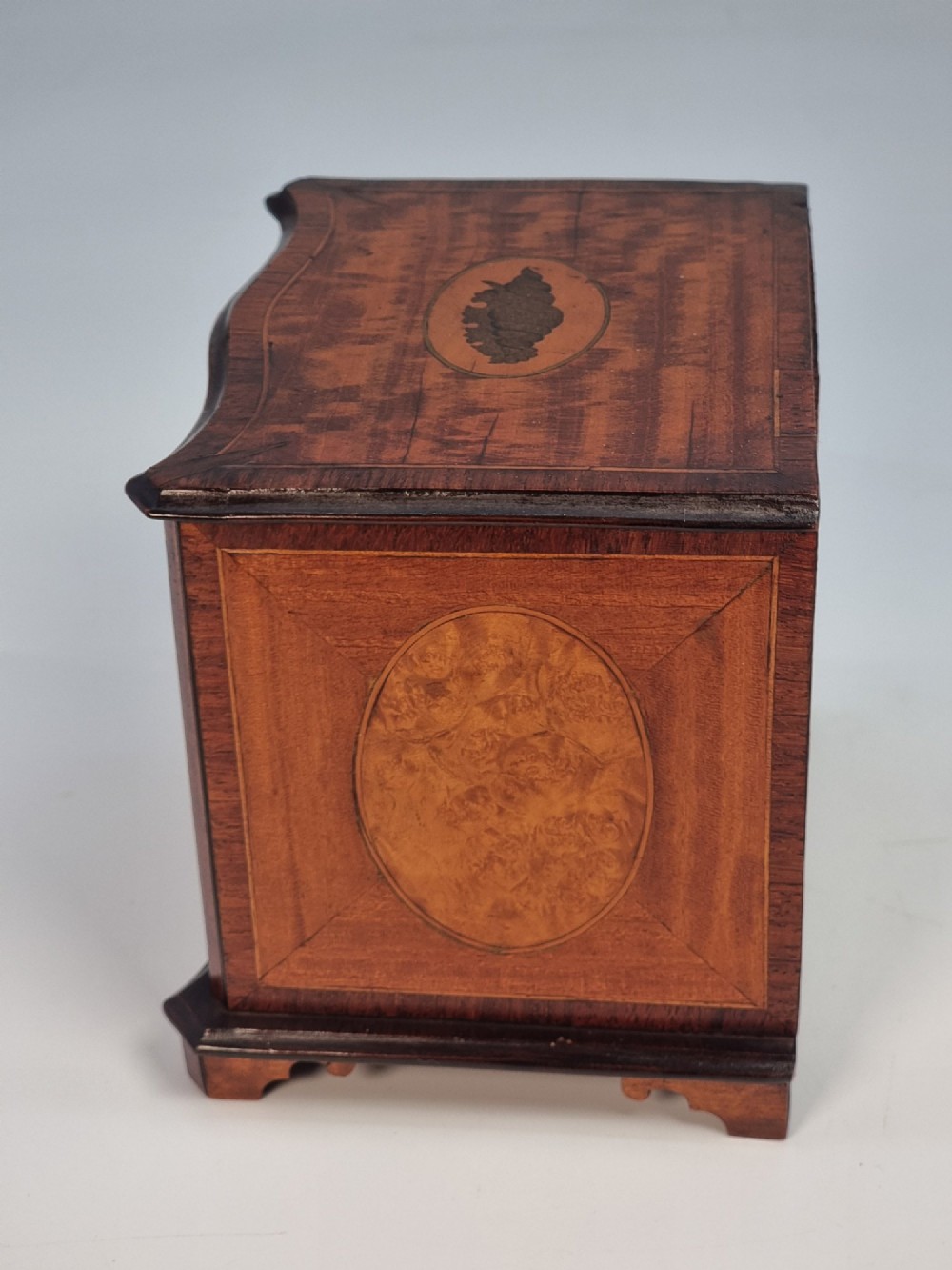 An Edwardian miniature satinwood chest of drawers featuring a serpentine front, inlaid shell medallion on the top, and four small drawers with wooden knobs. View V