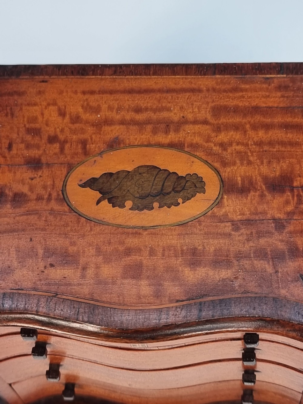 An Edwardian miniature satinwood chest of drawers featuring a serpentine front, inlaid shell medallion on the top, and four small drawers with wooden knobs. View IX